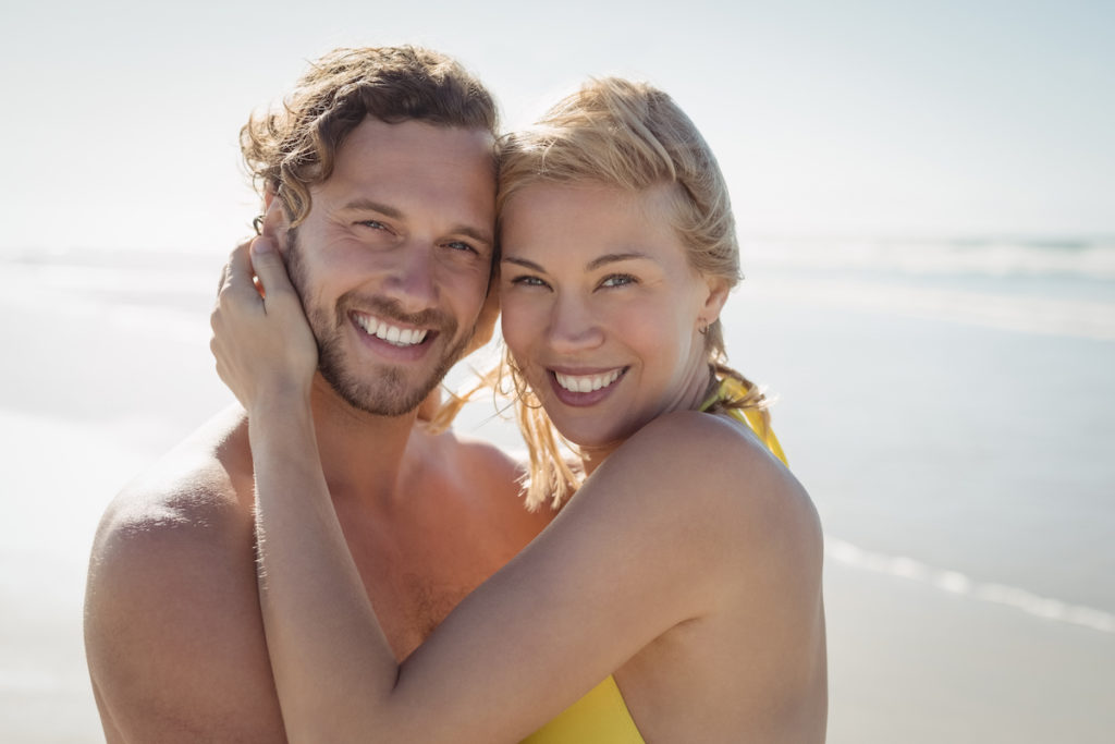 Portrait of smiling couple embracing at beach during sunny day