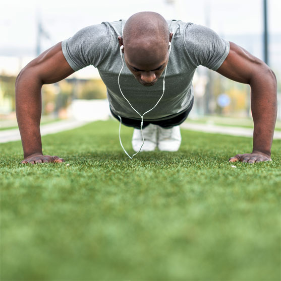 Healthy, Fit man doing pushups on grass wearing headphones