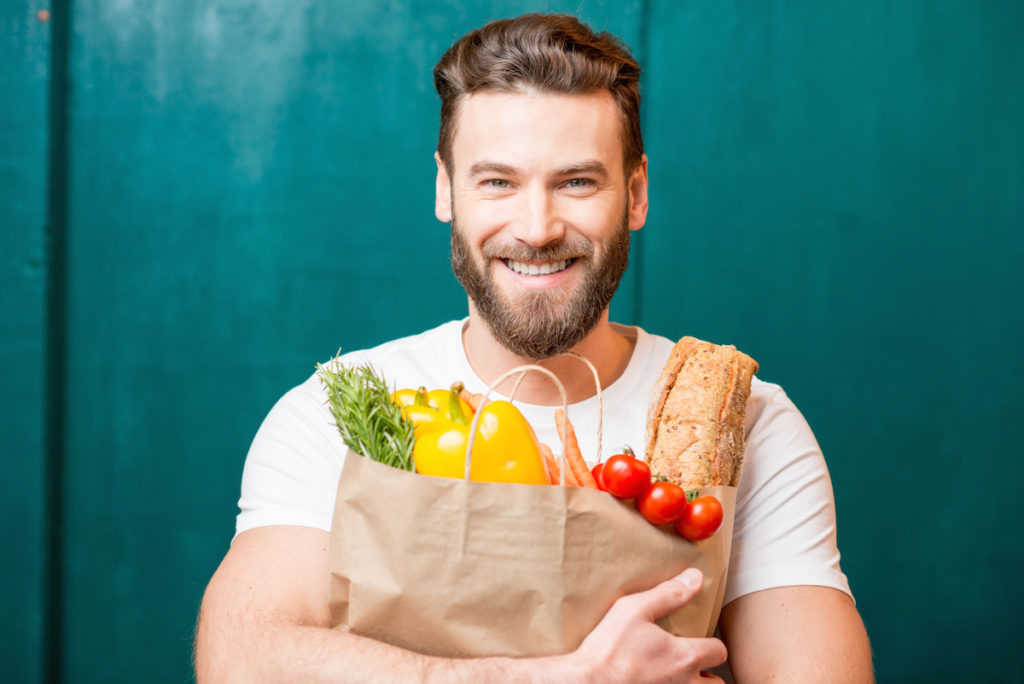Handsome man holding a paper bag full of healthy food on a green background